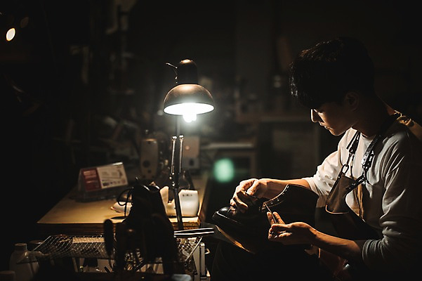 포토 JPG 응시 남자 신발 전등 실내 한명 사람 상반신 20대 옆모습 앞치마 한국인 작업실 가죽 신발끈 끼우기 수제화 가죽공방 국내포토 1 시선 뷰포인트 조명 동양인 청년 내부 공예 파일형식