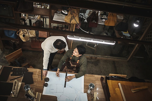 포토 JPG 직업 응시 남자 40대 중년 실내 대화 서기 미소 사람 앉기 상반신 20대 성인 두명 앞모습 하이앵글 마주보기 한국인 작업 가르침 작업실 제조 가죽 책상 스승 제자 실습 장인 가죽가방 가죽공예 제도기구 남자만 가죽공방 국내포토 시선 교육 뷰포인트 가구 가방 모션 표정 말하기 동양인 청년 내부 기구 공예 파일형식