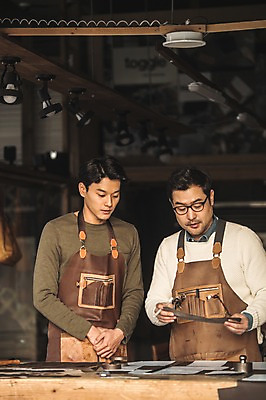 포토 JPG 직업 남자 40대 중년 실내 설명 서기 사람 상반신 20대 성인 두명 앞모습 한국인 작업 작업실 가죽 집중 책상 스승 제자 실습 장인 가죽공예 남자만 안경낌 가죽공방 국내포토 안경 뷰포인트 가구 컨셉 모션 동양인 청년 내부 공예 파일형식