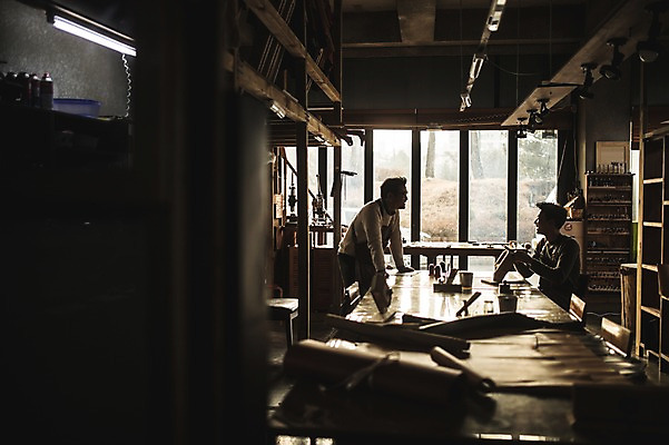 포토 JPG 직업 남자 40대 중년 실내 대화 설명 서기 미소 사람 앉기 상반신 20대 성인 두명 옆모습 마주보기 한국인 작업 가르침 작업실 제조 바느질 가죽 책상 역광 스승 제자 실습 장인 가죽공예 남자만 가죽공방 국내포토 교육 뷰포인트 가구 모션 표정 말하기 동양인 청년 내부 공예 파일형식