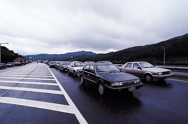 포토 JPG 주간 구름 시설물 현대건축 건축 도로 길 육상교통 교통수단 교통 가로등 교통시설 자동차 하늘 산 여러명 야외 트럭 고속도로 아스팔트 여러대 정체 차선_도로 국내포토 자연요소 건축물 공공시설 다수 사람 시설 파일형식